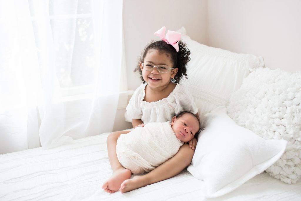 older sibling holding newborn baby.  organic all white newborn studio.  katie ballantine photography new market maryland baby photographer.  baby swaddled in white blanket.